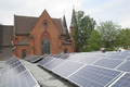 Solarzellen werden auf einem Flachdach installiert. Im Hintergrund ist die Friedenskirche zu sehen.