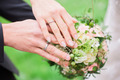 Ein Paar hält einen Hochzeitsstrauß und zeigt die Eheringe an seinen Händen.