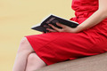 Eine Frau in einem roten Kleid hält eine Bibel auf dem Schoß
