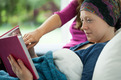 Das Symbolfoto zeigt eine lesende Frau im Bett eines Hospizes, mit einer Kopfbedeckung, weil sie offenbar keine Haare mehr hat