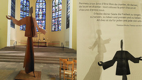 Eine große, abstrakte Skulptur eines aufrechten Menschen mit erhobenen Armen steht in einem Kirchenraum. Im Hintergrund befinden sich bunte Fenster. Neben der Skulptur ist ein Zitat zu sehen, das zur Freiheit des Singens, Tanzens und Liebens einlädt.