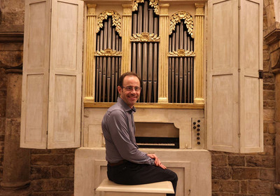 Auf dem Foto ist die Palmieri-Orgel im Bremer St. Petri Dom abgebildet. Davor auf der Orgelbank sitzt Domorganist Stephan Leuthold und blickt lächelnd in die Kamera.
