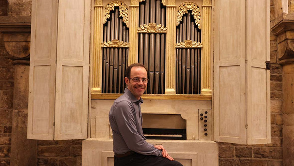 Auf dem Foto ist die Palmieri-Orgel im Bremer St. Petri Dom abgebildet. Davor auf der Orgelbank sitzt Domorganist Stephan Leuthold und blickt lächelnd in die Kamera.