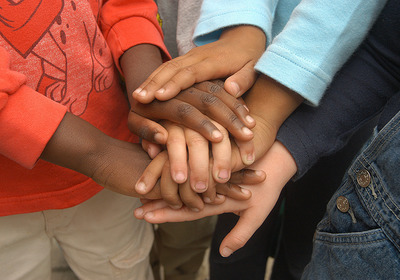 Das Foto zeigt Kinderhände in verschiedener Hautfarbe, die solidarisch übereinandergelgt werden