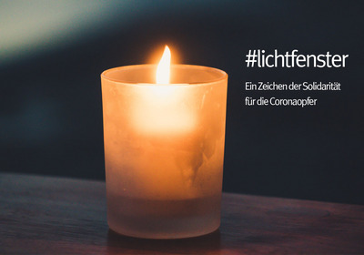 Eine brennende Kerze in einem gefrosteten Glas steht auf einem Tisch. Neben der Kerze steht der Text "#lichtfenster" und darunter "Ein Zeichen der Solidarität für die Coronaopfer". 