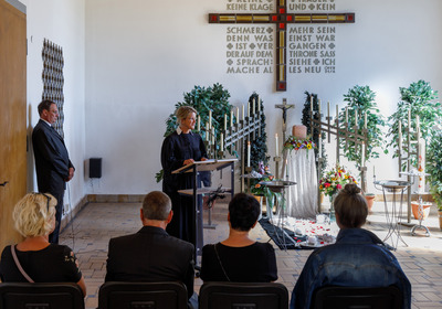 Ein Trauergottesdienst in einer Kirche. Gäste Altar mit Kreuz und eine Pfarrerin sind zu sehen.