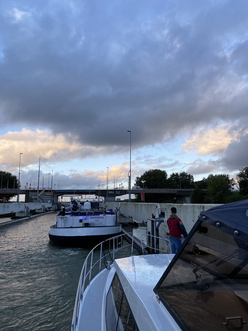 Der Blick an der Seite eines Bootes vorbei führt auf eine große Windschleuse, die sich das Boot mit einem großen Küstenmotorschiff teilt.