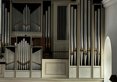Die Abbildung zeigt eine Orgel mit zahlreichen Metallpfeifen in verschiedenen Größen. Die Pfeifen sind in Gruppen angeordnet und verleihen der Orgel ein beeindruckendes, symmetrisches Aussehen. Der Hintergrund ist schlicht und lässt die Orgel in den Vordergrund treten.