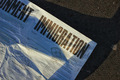 Ein zerknittertes Blatt Papier liegt auf dem Boden, mit dem Wort "IMMIGRATION" in großen, fetten Buchstaben. Darunter befinden sich verschiedene Textzeilen zu politischen Positionen und Vorschlägen in Bezug auf Einwanderung.
