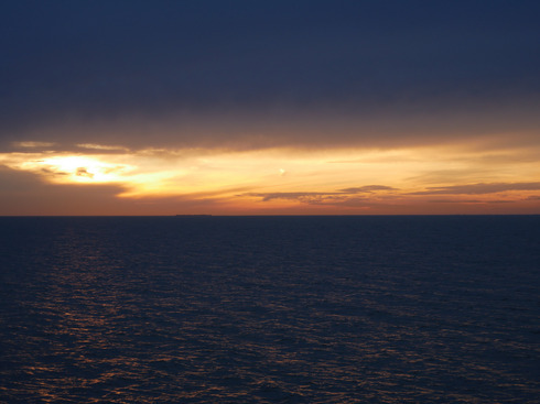 Ein goldener Sonnenuntergang wirkt sehr dramatisch über dunklem Wasser und aufziehenden Sturmwolken.