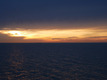 Ein goldener Sonnenuntergang wirkt sehr dramatisch über dunklem Wasser und aufziehenden Sturmwolken.