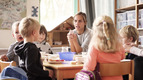 Die Erzieherin unterhält sich mit Kindergartenkindern an einem Tisch.