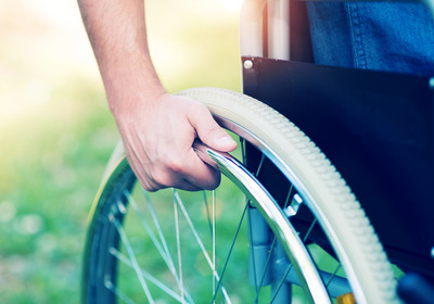 Eine Person hält ein Rad ihres Rollstuhls fest.