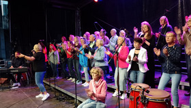 Eine Gruppe Menschen steht auf einer Musikbühne und singt gemeinsam