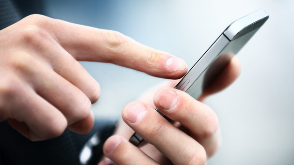 Das Foto zeigt eine Hand, die auf ein Handy tippt