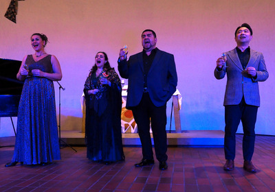 Zwei Opernsängerinnen und zwei Opernsänger singen mit einem Glas Sekt in der Hand