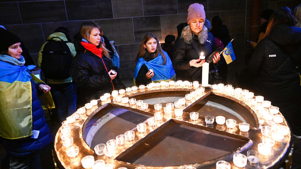 Das Bild zeigt Besucher eines Friedensgottesdienstes zum Gedenken an den Kriegsausbruch in der Ukraine. Einige Besucher haben sich in ukrainische Flaggen gehüllt.
