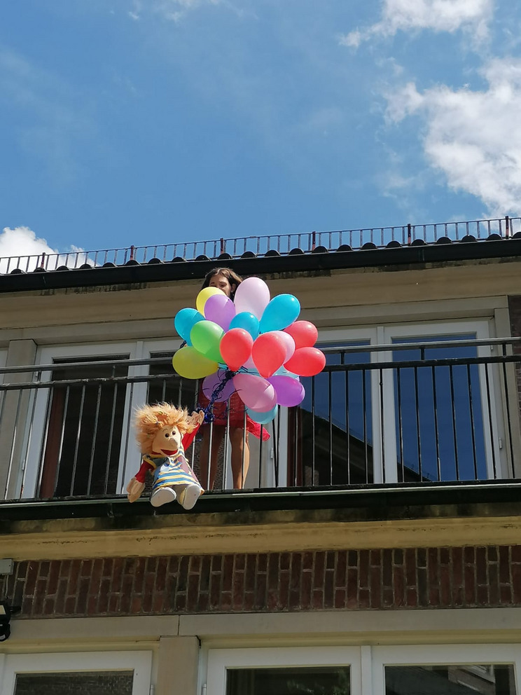 Man sieht die Handpuppe Violetta wie sie an ganz vielen Ballons festhält und scheinbar von einem Balkon fliegt.