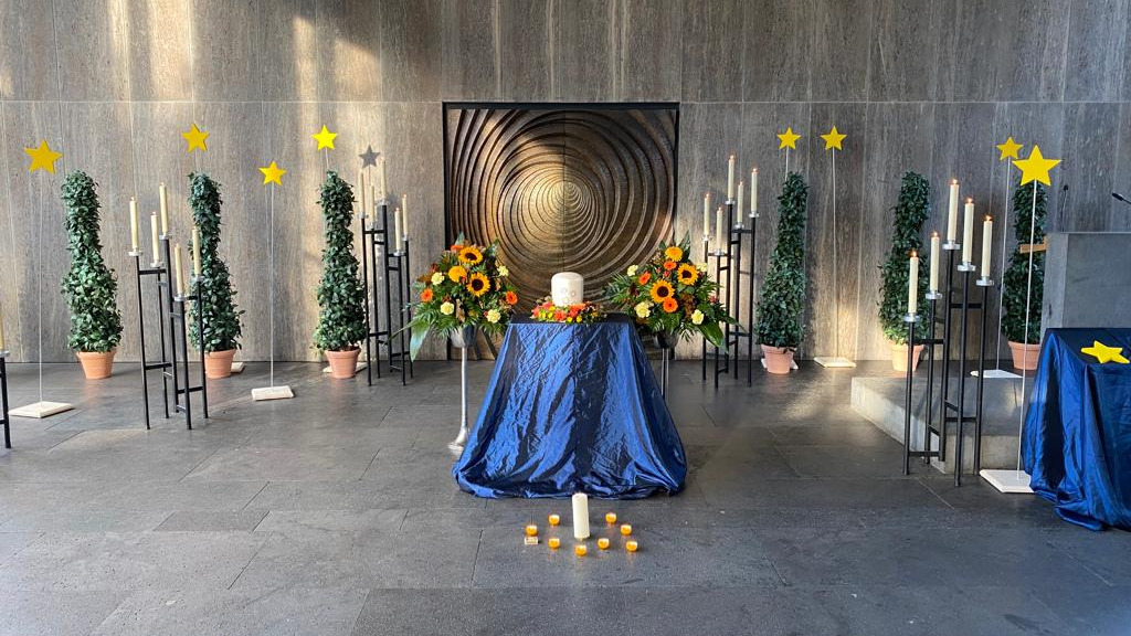 Innenansicht der Kapelle. Ein Altar, viele Kerzen und Blumengestecke befinden sich im Raum. Durch die Fenster scheint die Sonne.