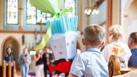 Ein Junge hält eine Schultüte in der Arm, es findet in der Kirche ein Einschulungsgottesdienst statt