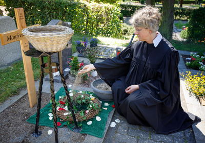 An einem Grab sitzt eine Person und führt ein Trauerritual aus.