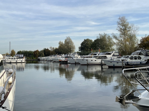 Ein Hafen mit vielen ähnlich aussehenden Schiffen liegt still bei blauem Himmel.