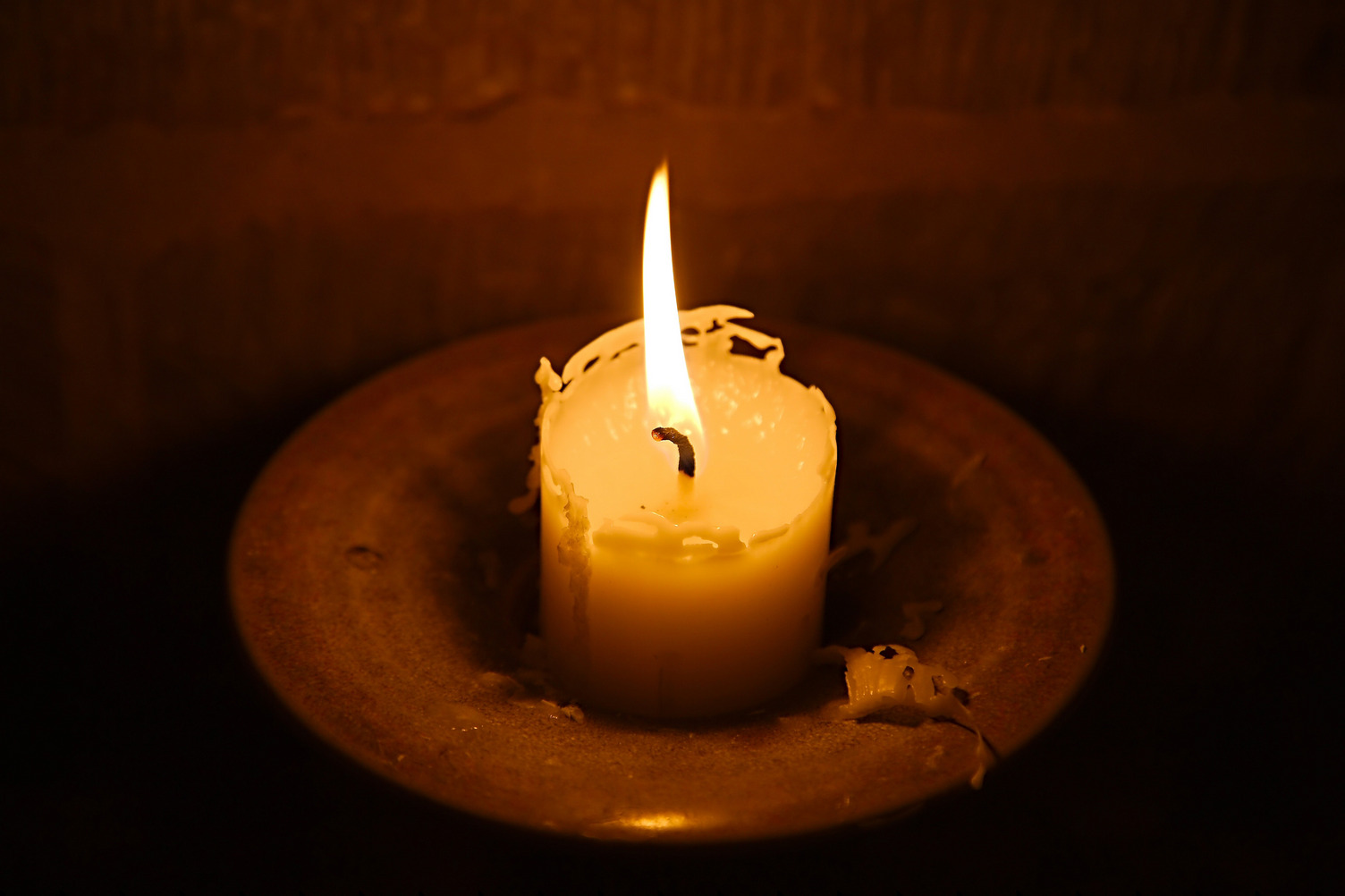 Eine Kerze scheint in einem dunklen Raum. Die Kerz ist schon sehr weit heruntergebrannt.