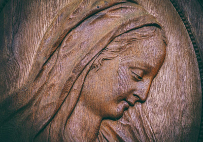 Eine Holzschnitzerei zeigt das Profil einer Dame mit sanftem Ausdruck. Ihr Gesicht ist von einer feinen Haarsträhne umrahmt, und die Details ihrer Gesichtszüge und das Material verleihen der Darstellung Warmherzigkeit und Tiefe.