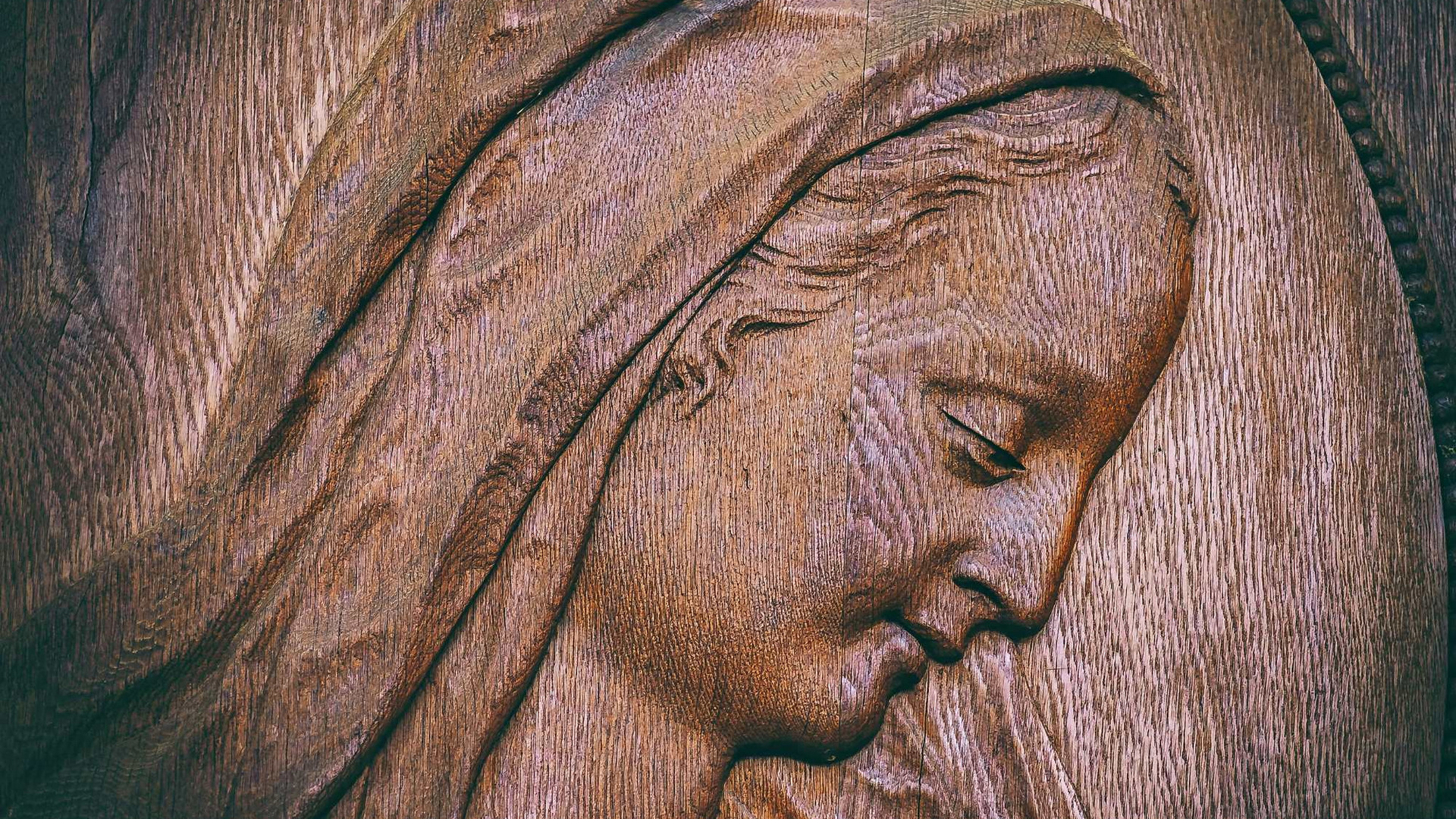 Eine Holzschnitzerei zeigt das Profil einer Dame mit sanftem Ausdruck. Ihr Gesicht ist von einer feinen Haarsträhne umrahmt, und die Details ihrer Gesichtszüge und das Material verleihen der Darstellung Warmherzigkeit und Tiefe.