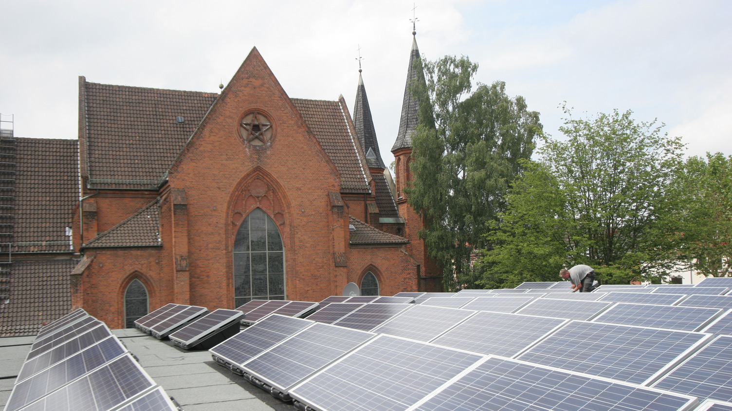 Solarzellen werden auf einem Flachdach installiert. Im Hintergrund ist die Friedenskirche zu sehen.