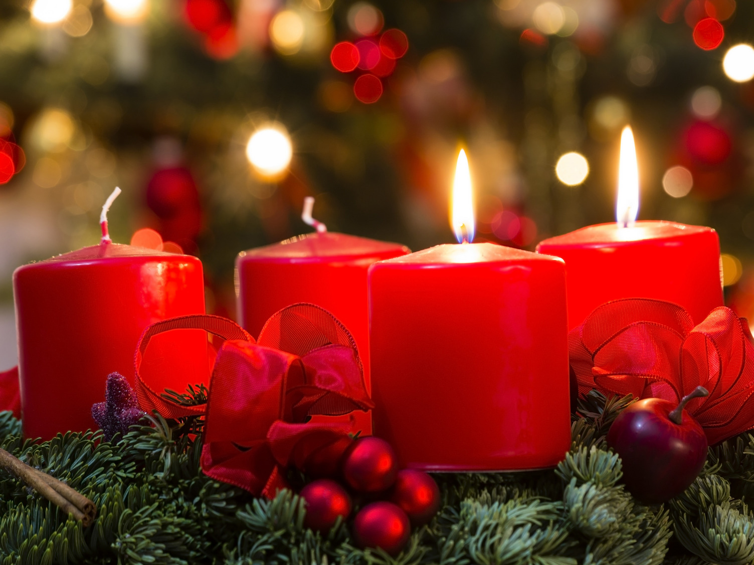 Ein Adventskranz aus Tannenzweigen mit 4 roten Kerzen. Der Kranz ist mit roten Schleifen geschmückt.