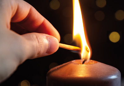 Eine Hand entzündet eine Kerze