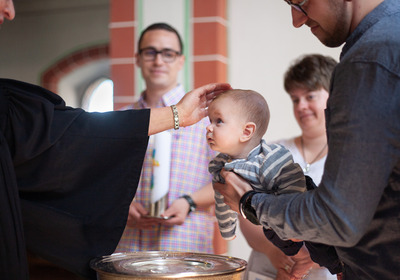 Ein Baby wird am Taufbecken einer Kirche getauft.