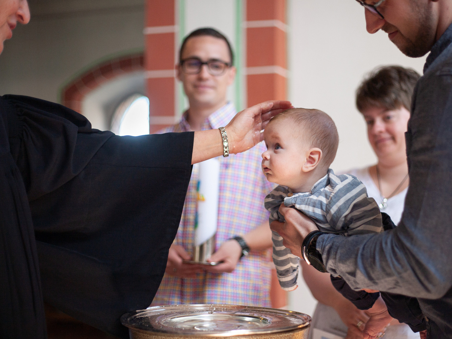 Ein Baby wird am Taufbecken einer Kirche getauft.