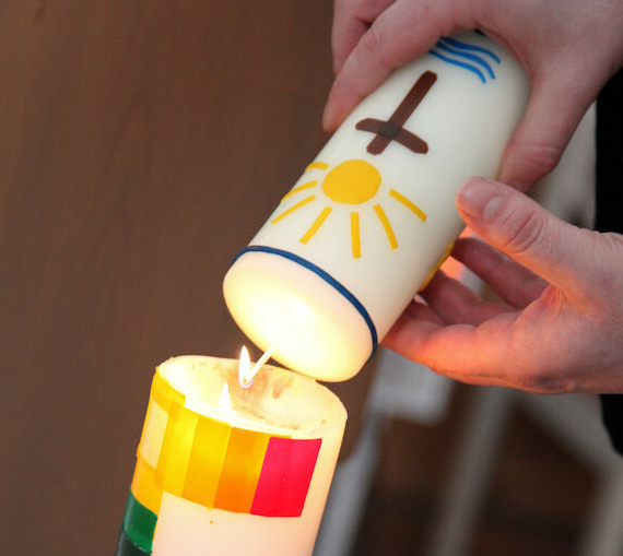Osterkerze mit buntem Kreuz. Taufkerze schräg darüber mit Sonne, Kreuz und Wasser.