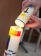 Osterkerze mit buntem Kreuz. Taufkerze schräg darüber mit Sonne, Kreuz und Wasser.