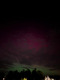 Nordlichter in pink und grün am Himmel über einem Hafen.