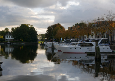 Eine Reihe von Booten liegen in einem Hafen und spiegeln sich im Wasser.