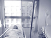 Ein Person liegt starr in einem Krankhausbett, im Vordergrund steht ein Infusionsständer.