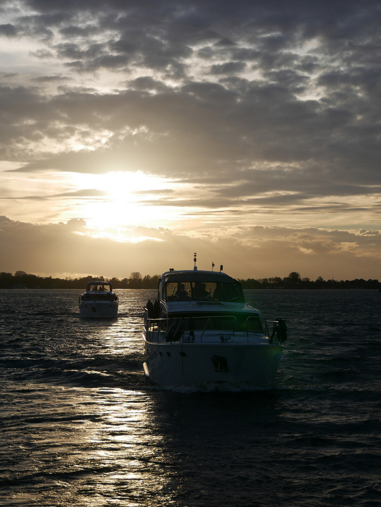 Sonnenuntergang Joure Zwei Motorboote fahren bei Sonnenuntergang über das Wasser. Die untergehende Sonne erhellt den Himmel, der mit Wolken bedeckt ist. Die Wellen reflektieren das Licht der tiefstehenden Sonne und schaffen eine ruhige, entspannte Atmosphäre.