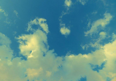 Der Himmel zeigt eine sanfte Mischung aus blauen und weißen Wolken vor einem klaren, hellen Hintergrund. Die Wolken sind locker verteilt und variieren in Form und Größe, was eine beruhigende und offene Atmosphäre schafft.