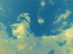 Der Himmel zeigt eine sanfte Mischung aus blauen und weißen Wolken vor einem klaren, hellen Hintergrund. Die Wolken sind locker verteilt und variieren in Form und Größe, was eine beruhigende und offene Atmosphäre schafft.