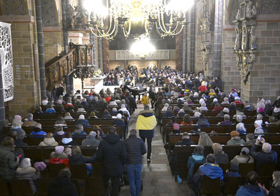Das Bild zeigt Besucher eines Friedensgottesdienstes im Bremer St. Petri Dom zum Gedenken an den Kriegsausbruch in der Ukraine. Einige Besucher haben sich in ukrainische Flaggen gehüllt.