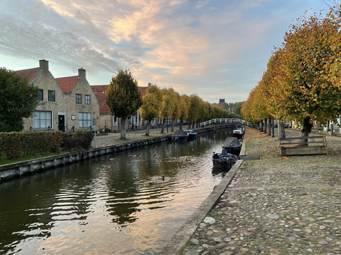 Ein Kanal in Sloten eingerahmt von Häusern und gelben Bäumen während die Sonne untergeht.