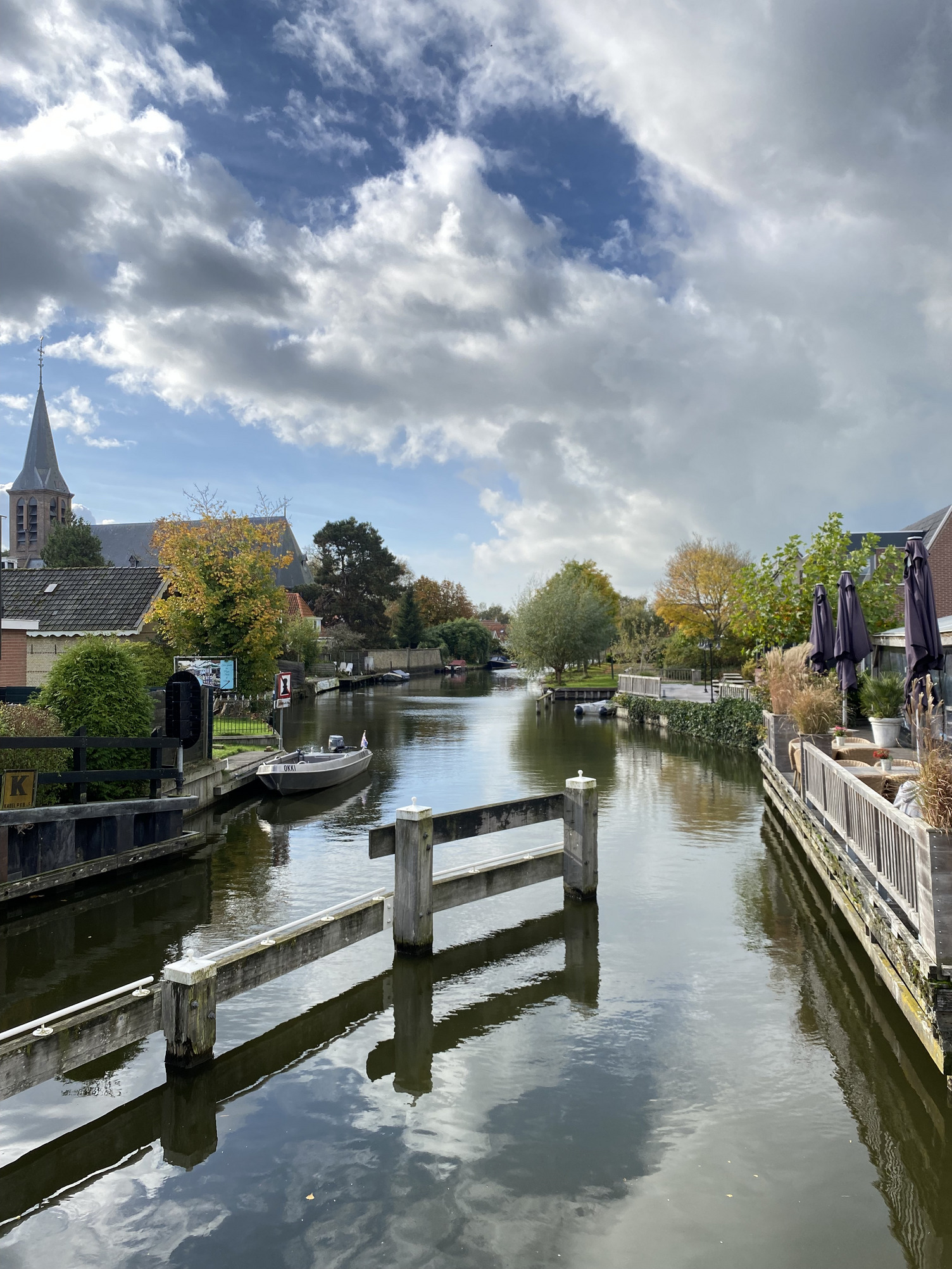Der Blick führt auf einer Brücke einen Kanal hinunter der durch den Ort fließt. Die Wolken am blauen Himmel spiegeln sich auf der Wasseroberfläche.