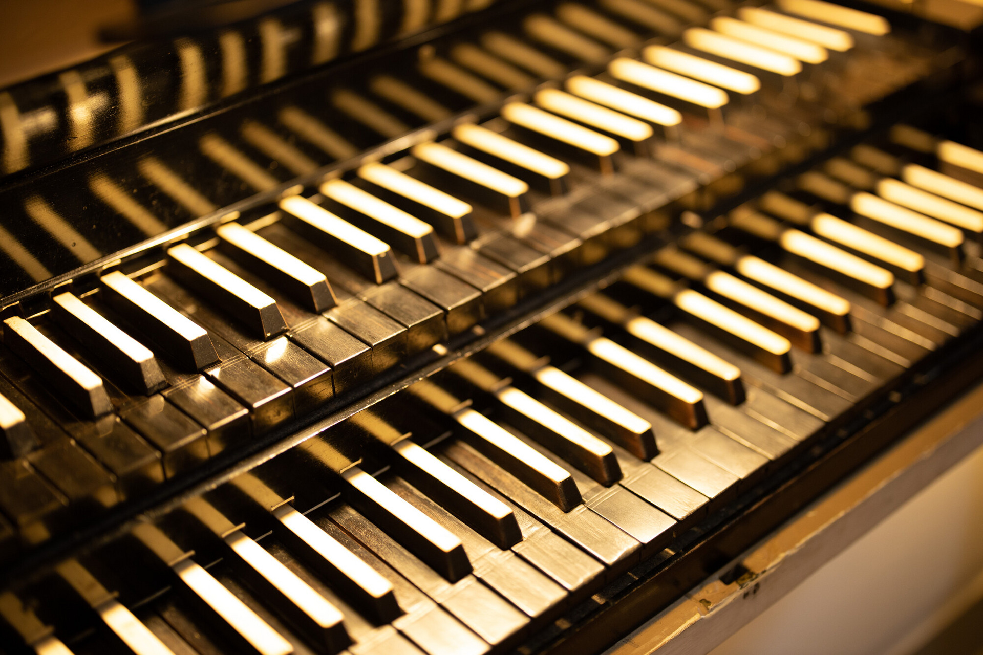 Die Abbildung zeigt eine Nahaufnahme von Tasten eines Musikinstruments, vermutlich einer Orgel oder einem Klavier. Die Tasten sind in verschiedenen hellen und dunklen Farbtönen angeordnet, wobei einige glänzende Details sichtbar sind. Die Bildkomposition hebt die feinen Strukturen der Tasten hervor.