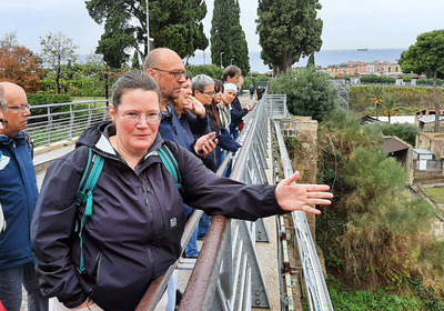Eine Frau erklärt einer Gruppe etwas in einer archäologischen Ausgrabung