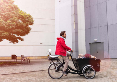 Das Foto zeigt einen Mann mit roter Jacke auf einem Lastenfahrrad.