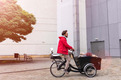 Das Foto zeigt einen Mann mit roter Jacke auf einem Lastenfahrrad.