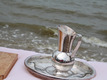 Da Foto zeigt ein silbernes Taufgeschirr mit Krug und Schale vor dem Hintergrund des Weserufers.
